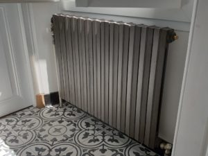 Photo d'un radiateur gris en fonte sous une fenêtre